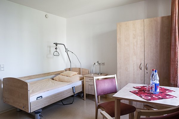 Helles Einzelzimmer des Nellinistrifts mit Pflegebett, Nachttisch, Tisch und Kleiderschrank