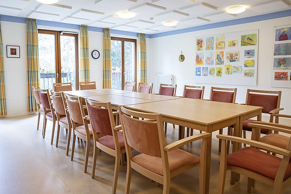 Heller Gemeinschaftsraum mit 6 zu einem großen Tisch zusammengestellten Holztischen, umgeben von Stühlen