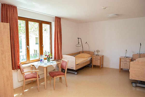 Geräumiges Zimmer mit 2 Pflegebetten, Nachttischen, sowie einem Tisch vor dem Fenster