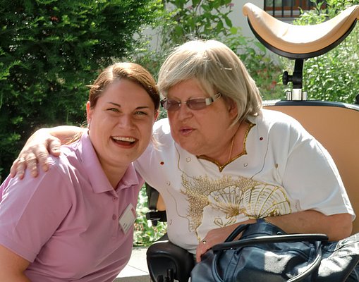 Eine Bewohnerin und eine Mitarbeiterin – Arm in Arm nebeneinander 