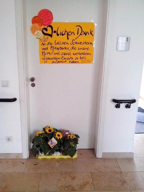 Blumen und eine Danksagung an der Tür des Personals des Nellinistifts. Aufschrift: 'Herzlichen Dank an die tollen Schwestern und Mitarbeiter, die unsere Mutter mit soviel wertvollem und liebevollem Einsatz so toll aufgebaut haben.'